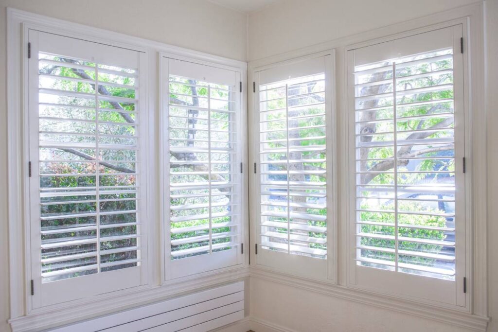 Classic Shutters Open to a Sunny Front Yard with Trees and Bushes
